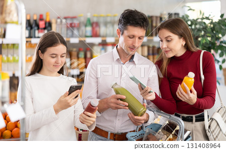 Family with teenage girl scanning QR on bottle of smoothie in supermarket Family with teenage girl scanning QR on bottle of smoothie in supermarket 131408964