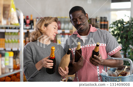 African man with European wife hold bottle and choose alcohol, wine or beer bottle in store African man with European wife hold bottle and choose alcohol, wine or beer bottle in store 131409008