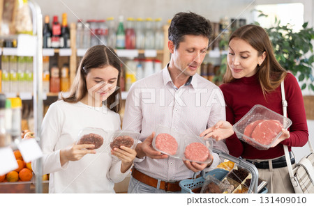 Dad, mom and daughter choose raw chilling beef entrecote and semi-finished hamburger cutlet in shop Dad, mom and daughter choose raw chilling beef entrecote and semi-finished hamburger cutlet in shop 131409010