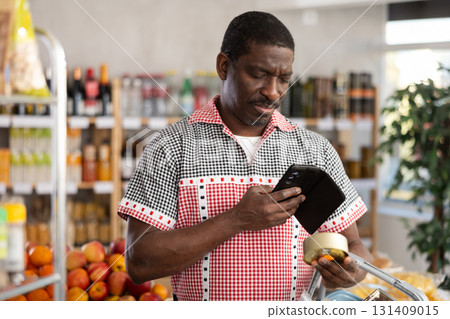 African man customer at shop scans QR code on tin cans of preserves using phone camera 131409015