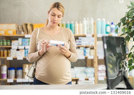 Pregnant woman customer choosing ointment in box in drugstore Pregnant woman customer choosing ointment in box in drugstore 131409016