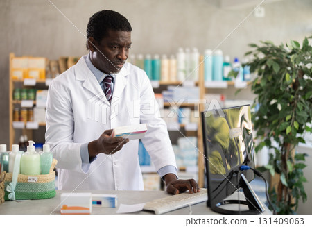 Male pharmacist looking for pills on computer Male pharmacist looking for pills on computer 131409063
