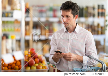 Adult man with phone choosing groceries in store Adult man with phone choosing groceries in store 131409090