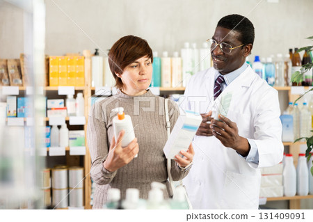 Woman choose buy emollient cream at pharmacy. African man in background Woman choose buy emollient cream at pharmacy. African man in background 131409091