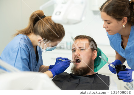 Two women dentists treating a man teeth Two women dentists treating a man teeth 131409098