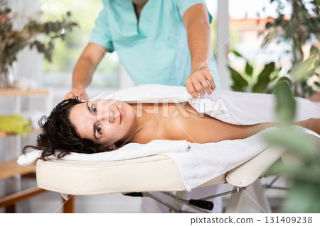 Male massage therapist carefully covers young relaxed woman with veil after massage 131409238