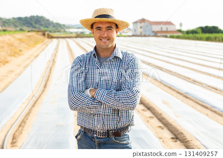 Smiling farmer standing on plantation mulched with polyethylene film 131409257