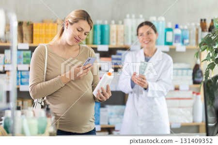 Pregnant woman in pharmacy scans QR code on antifungal cream, pharmacist offer similar product in background. Pregnant woman in pharmacy scans QR code on antifungal cream, pharmacist offer similar product in background. 131409352