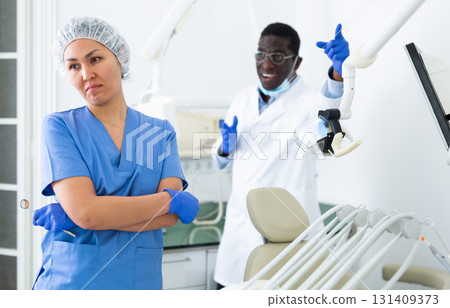 Frustrated female dental assistant standing in office with disgruntled doctor 131409373