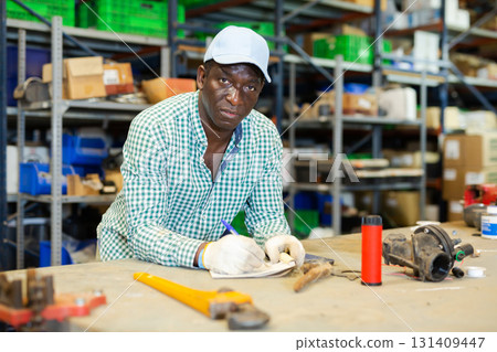 Storehouse worker standing at workbench and making notes Storehouse worker standing at workbench and making notes 131409447
