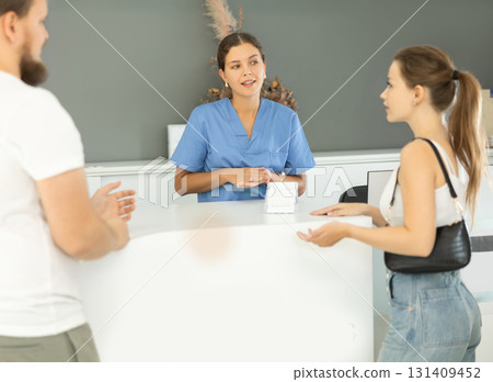 Dental clinic administrator talks to patients at reception desk Dental clinic administrator talks to patients at reception desk 131409452