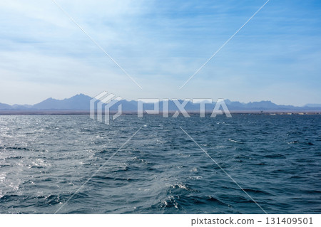 Serene ocean waves and distant mountain landscape under clear blue sky Serene ocean waves and distant mountain landscape under clear blue sky 131409501