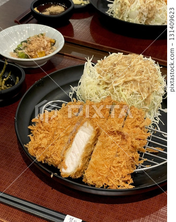 Crispy tonkatsu, a Japanese-style breaded and deep-fried pork cutlet, served with shredded cabbage and drizzled with savory sauce. A delightful balance of crunchy texture and juicy meat. Crispy tonkatsu, a Japanese-style breaded and deep-fried pork cutlet, served with shredded cabbage and drizzled with savory sauce. A delightful balance of crunchy texture and juicy meat. 131409623