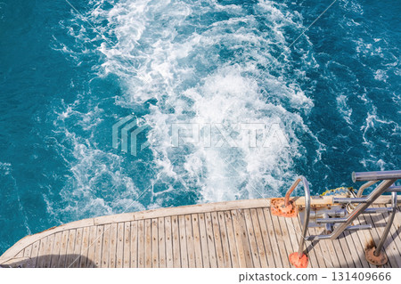Boat deck overlooking turquoise ocean waters with wake trails for nautical themes 131409666