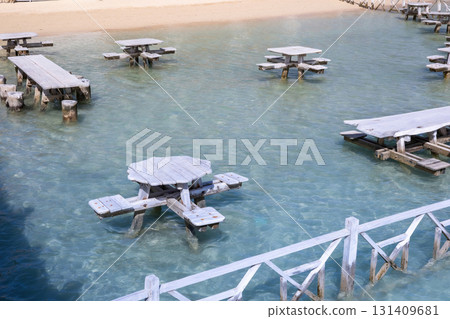 Unique outdoor seating area with wooden picnic tables above clear water by sandy beach 131409681