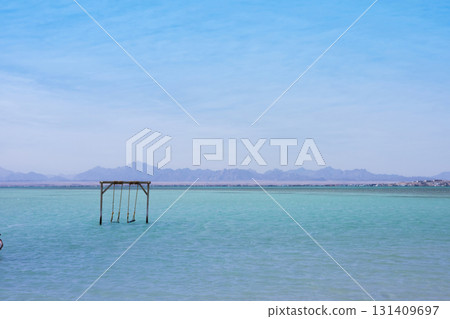 Tranquil seaside scene with wooden swing set against distant mountains Tranquil seaside scene with wooden swing set against distant mountains 131409697