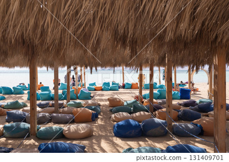 Relaxing beach lounge with colorful bean bags under straw umbrellas - ideal summer getaway Relaxing beach lounge with colorful bean bags under straw umbrellas - ideal summer getaway 131409701