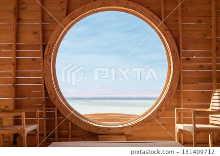 Tranquil indoor space with large circular window overlooking serene sea and distant mountains Tranquil indoor space with large circular window overlooking serene sea and distant mountains 131409712