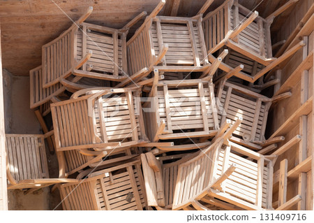 Rustic wooden chairs stacked in sunlit storage space for outdoor seating arrangement inspiration Rustic wooden chairs stacked in sunlit storage space for outdoor seating arrangement inspiration 131409716