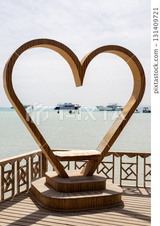 Heart-shaped sculpture overlooking tranquil sea with boats in the distance 131409721