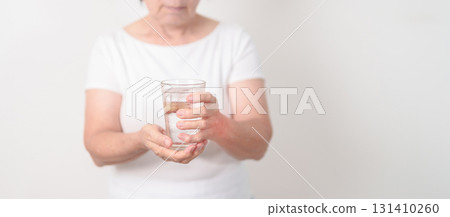 Elderly woman having Tremor hand during hold water glass. Parkinson disease April awareness month, Carpal Tunnel Syndrome, rheumatoid and brain injury, Neurological disorder and Senior health concept Elderly woman having Tremor hand during hold water glass. Parkinson disease April awareness month, Carpal Tunnel Syndrome, rheumatoid and brain injury, Neurological disorder and Senior health concept 131410260