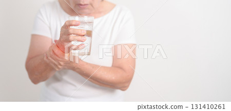 Elderly woman having Tremor hand during hold water glass. Parkinson disease April awareness month, Carpal Tunnel Syndrome, rheumatoid and brain injury, Neurological disorder and Senior health concept 131410261