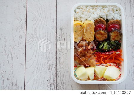 A photo of a healthy, home-style, nutritionally balanced bento box containing tamagoyaki (rolled omelet) and fried chicken placed on a wood-grain table. A photo of a healthy, home-style, nutritionally balanced bento box containing tamagoyaki (rolled omelet) and fried chicken placed on a wood-grain table. 131410897