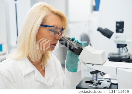Scientists performing detailed medical research using a microscope in a modern laboratory setting.  131411439