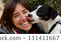 Smiling woman shares a joyful moment as her dog affectionately licks her cheek 131411667