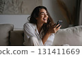 Smiling woman relaxing on sofa with smartphone, enjoying a joyful carefree moment 131411669