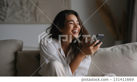 Smiling woman relaxing on sofa with smartphone, enjoying a joyful carefree moment 131411669