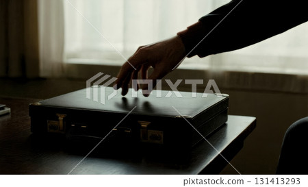 A person's hand reaching for a briefcase in a dark room. Conspiracy, secret meeting, briefcase, mystery, thriller. 131413293