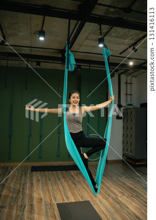 Female performing aerial yoga stretch using fabric hammock in modern studio Female performing aerial yoga stretch using fabric hammock in modern studio 131416113