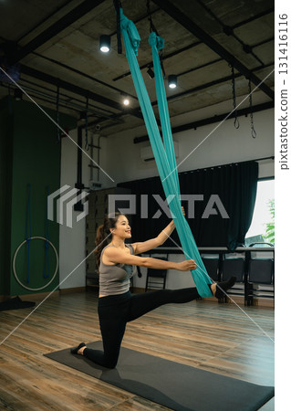 Young woman exercising with aerial yoga silk hammock, focusing on strength, posture, and mindfulness 131416116