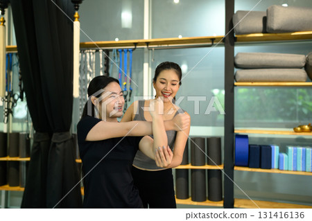 Fitness instructor helping woman stretch arm muscles during personal training session in yoga studio Fitness instructor helping woman stretch arm muscles during personal training session in yoga studio 131416136