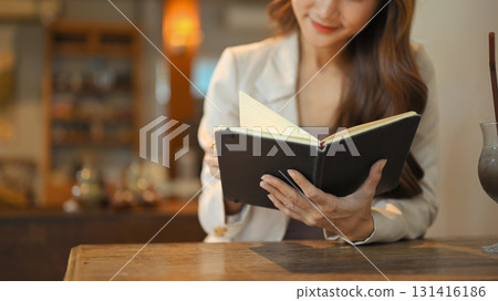 Close up of woman in beige suit reading and reviewing notes in a notebook at a wooden table 131416186