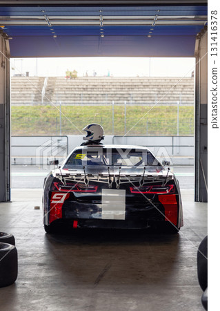 Scenic view powerful racecar stands inside pit garage with helmet placed on roof, ready for action on racing track. Back rear view aerodynamic details, performance design, motorsport atmosphere Scenic view powerful racecar stands inside pit garage with helmet placed on roof, ready for action on racing track. Back rear view aerodynamic details, performance design, motorsport atmosphere 131416378
