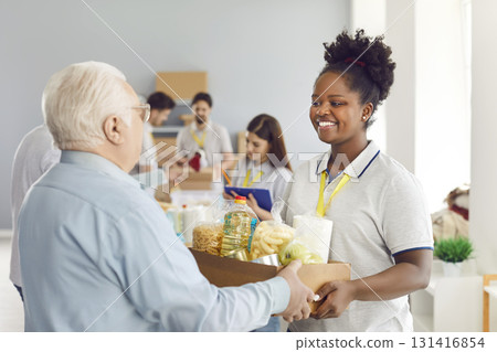 African American woman volunteer giving food box to elderly man, close-up 131416854