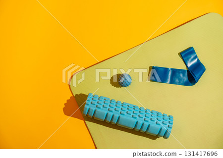 Foam roller massage ball and single blue band on green mat over yellow background minimal fitness tools 131417696