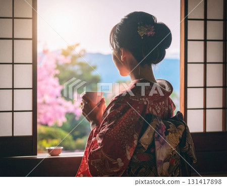 A woman in a kimono drinking tea while looking at the scenery outside 131417898