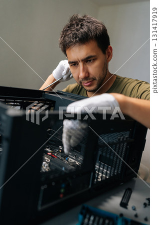 Vertical portrait of thoughtful computer technician wearing white gloves meticulously repairing desktop pc with screwdriver in workshop. Concept of computer hardware, repairing, upgrade and technology 131417919