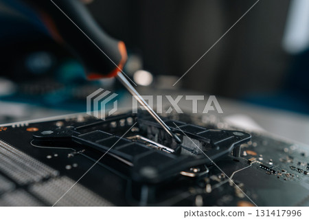 Skilled technician carefully removing aged thermal paste from computer motherboard CPU socket, readying precise surface for processor replacement. Concept of desktop PC maintenance and service. Skilled technician carefully removing aged thermal paste from computer motherboard CPU socket, readying precise surface for processor replacement. Concept of desktop PC maintenance and service. 131417996