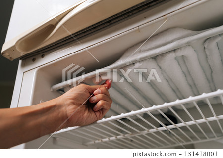 Low-angle view of housekeeper removing ice buildup from freezer compartment of refrigerator, highlighting need for regular defrosting and cleaning to maintain optimal appliance performance. Low-angle view of housekeeper removing ice buildup from freezer compartment of refrigerator, highlighting need for regular defrosting and cleaning to maintain optimal appliance performance. 131418001