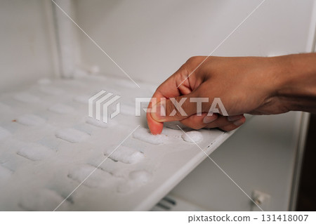 Close-up cropped shot of unrecognizable man touching ice formation on shelf within refrigerator freezer compartment during maintenance home appliance. Concept of defrosting due to excessive buildup Close-up cropped shot of unrecognizable man touching ice formation on shelf within refrigerator freezer compartment during maintenance home appliance. Concept of defrosting due to excessive buildup 131418007