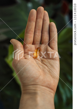 Single omega softgel in an open palm with green plant background 131418010