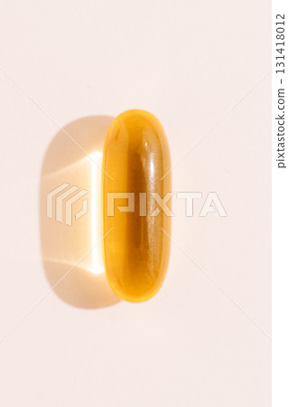 Golden softgel pill vertical macro isolated with glassy highlight on neutral background clean beauty wellness Golden softgel pill vertical macro isolated with glassy highlight on neutral background clean beauty wellness 131418012