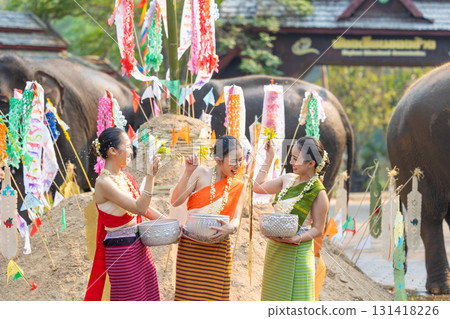 Songkran festival. Northern Thai people in Traditional clothes dressing splashing water together in Songkran day cultural festival with sand pagoda and colorful paper flag. 131418226