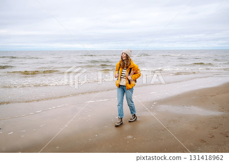 A beautiful young tourist woman in a yellow jacket with a backpack enjoys life near the sea. Travel. 131418962