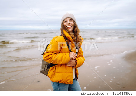 A beautiful young tourist woman in a yellow jacket with a backpack enjoys life near the sea. Travel. A beautiful young tourist woman in a yellow jacket with a backpack enjoys life near the sea. Travel. 131418963