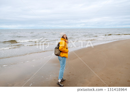 A beautiful young tourist woman in a yellow jacket with a backpack enjoys life near the sea. Travel. 131418964